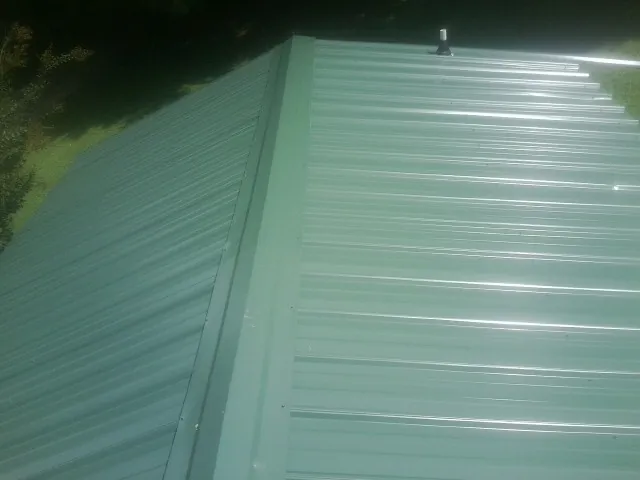 New green metal panels meeting at the ridge of a roof — Flat Roof Repair work by our crew in Swanton