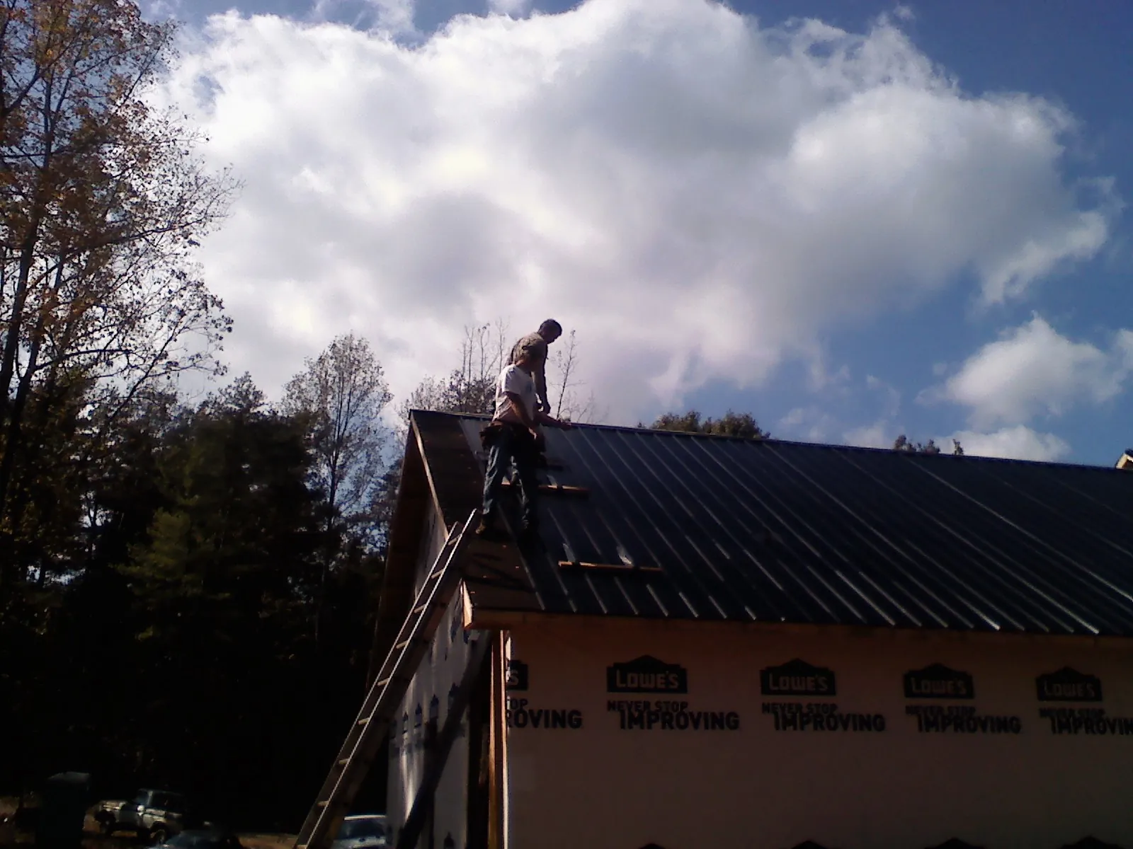 Roofer fastening dark metal panels high against a cloudy sky, from a Roof Inspection job in Swanton