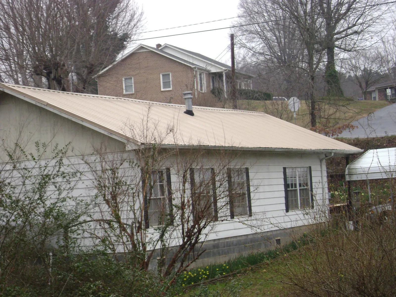 Tan metal roof on a white sided house set into a hillside — Commercial Roofing by Roofing Brothers in Swanton