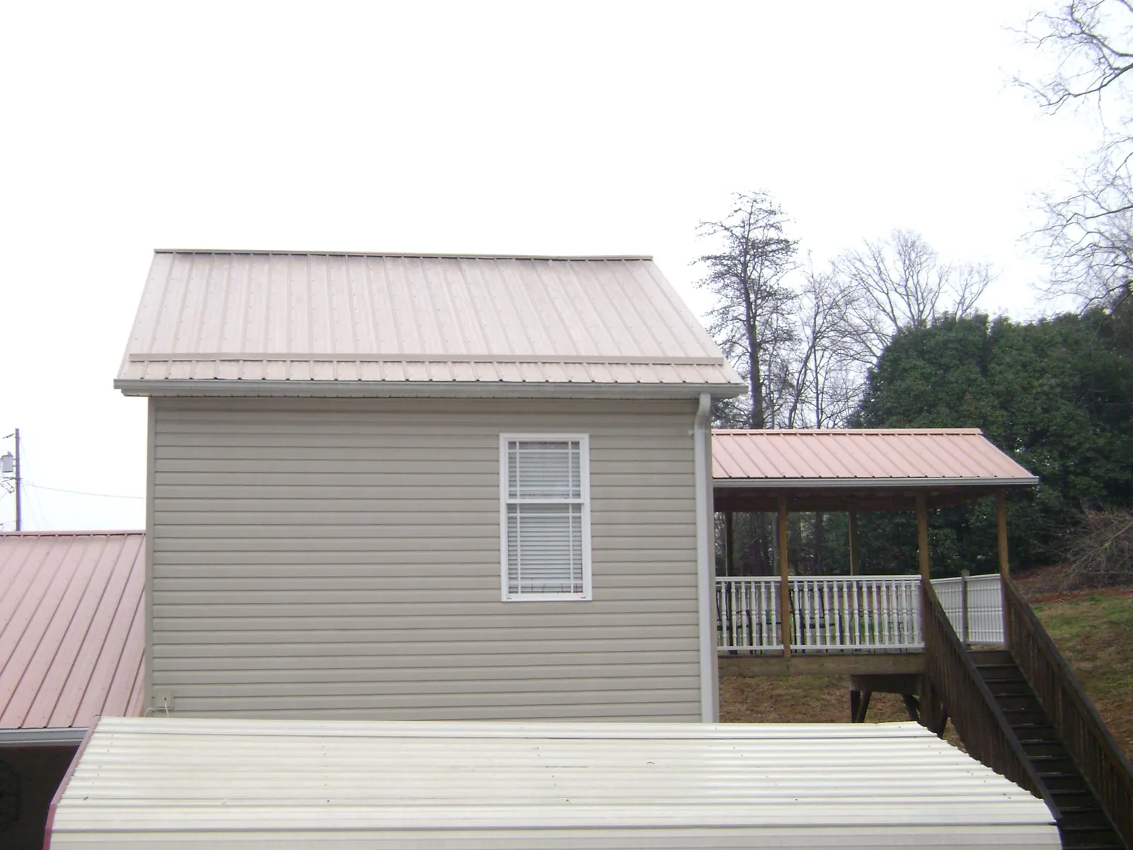 Tan metal roofs on a two story addition and attached porch, from a Roof Replacement job in Swanton